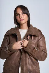 Campera gamulán marrón de símil cuero, con interior de corderoy al tono, cierre frontal con cremallera y cuello con solapas grandes. Presenta detalles de hebillas en los puños y bolsillos laterales con cierre.
