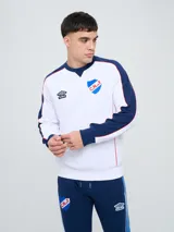 Buzo deportivo azul marino con detalles en rojo y blanco en cuello, hombros y mangas, de cuello redondo y manga larga, con el logo de Umbro y el escudo del Club Nacional de Football bordados en el pecho.