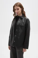 Sobrecamisa de cuero sintético color negro, con cuello clásico, cierre frontal con botones metálicos a presión, manga larga con puños rectos y un bolsillo frontal en el pecho.