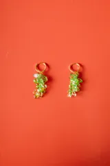 Aro tipo argolla dorada con colgante en forma de racimo de uvas, compuesto por pequeñas cuentas de cristal verde y hojas metálicas doradas.