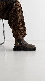 Botas de caña baja con punta cuadrada, confeccionadas en una combinación de cuero liso y gamuza en tonos marrones. Presentan un diseño con múltiples cortes y costuras visibles, cierre elástico lateral y suela de goma dentada tipo track.