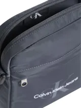 Bandolera Calvin Klein Jeans gris con logo estampado en el frente, bolsillo externo con cierre y correa ajustable.