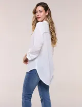 Camisa Magaschoni de silueta holgada y tejido texturizado color blanco, con cuello camisero, cierre frontal de botones, mangas largas con presilla para arremangar y diseño asimétrico con espalda más larga.
