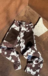 Pantalón vaquero de corte recto con estampado animal print tipo vaca en tonos marrón y blanco, con bolsillos delanteros de tela lisa y aberturas en los tobillos.