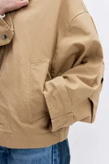 Cazadora de corte oversize en color beige, con cuello de solapa en contraste de color oscuro, cierre frontal con botones y bolsillos laterales.