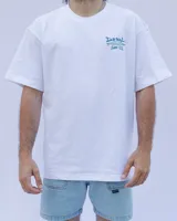 Remera blanca de algodón con cuello redondo y estampado en el pecho con el texto "Denali Surf Co." y una tabla de surf.