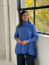 Sweater de punto color azul, con cuello alto acanalado, mangas largas y diseño holgado con costuras verticales decorativas.