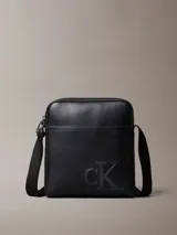 Bandolera reporter Calvin Klein de poliuretano color negro, con correa ajustable al hombro, cierre superior con cremallera, bolsillo frontal externo y logo monograma grabado en la parte inferior.