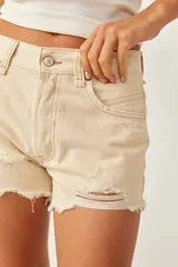 Short de denim color beige, de tiro medio y silueta relajada, con cinco bolsillos, cierre frontal con botón y cremallera, y detalles de roturas y bordes deshilachados.