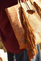 Bolso maxi de cuero marrón con textura croco, flecos laterales y botón de guampa. Tiene bolsillo interior y cierre metálico.