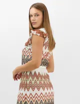 Vestido midi confeccionado en tejido de punto calado, con patrón geométrico en zigzag en tonos blanco, marrón, tostado y azul. Presenta escote a la base, mangas cortas con volados en los hombros, silueta recta y forro interior a tono. Incluye un cinturón fino con hebilla metálica.