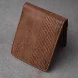 Billetera plegable de eco cuero azul, con múltiples compartimentos para tarjetas, monedero con cierre, tarjetero con visor y dos espacios para billetes. Presenta líneas de pespunte decorativas en la parte superior y el logo de la marca grabado en la esquina inferior.