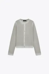 Chaqueta de punto de manga larga y cuello redondo, color gris claro con un sutil brillo metálico y efecto degradado en el tejido. Cierre frontal con botones plateados.