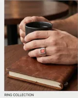 Anillo de acero tipo sello con piedra central rectangular de color rojo y diseño grabado en los laterales.