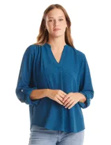 Blusa de manga larga con escote en V y detalle de presilla con botón para regular el largo de las mangas. Presenta una textura sutil en la tela y un corte holgado.