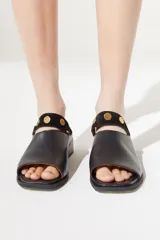 Sandalia de cuero color beige, con diseño slip on y detalle de tachas doradas.