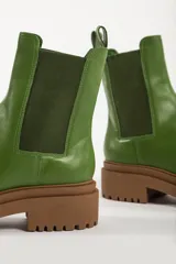 Bota tipo chelsea con suela track de goma en color marrón y capellada de cuero negro. Presenta elásticos laterales y tirador trasero.
