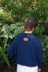 Sweater de tejido de punto acanalado en color marrón, con cuello redondo, mangas largas y bordado distintivo en color rojo en el pecho.