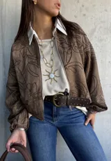 Campera tipo bomber de gamuza color marrón, con diseño bordado de motivos florales en toda la prenda. Presenta cierre frontal, cuello redondo y mangas largas con puños elásticos.