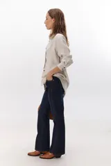 Camisa beige de manga larga con botones marrones y cuello clásico. Presenta un detalle de costura dorada a lo largo de la botonera.