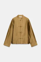 Camisa de estilo oriental confeccionada en mezcla de lyocell con acabado satinado. Presenta cuello redondo, manga larga con puños rectos, bolsillos de plastrón y cierre frontal mediante alamares.