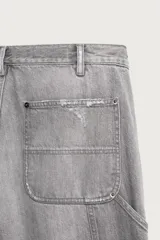 Jeans relaxed fit de tiro medio y pernera recta confeccionados en denim de algodón rígido, con diseño de carpintero que incluye bolsillos superpuestos y roturas localizadas en el frente.