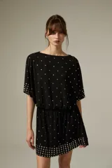 Vestido corto de poliéster color negro con escote a la base, mangas cortas y diseño holgado. Cuenta con detalles de tachas metálicas plateadas distribuidas por la prenda y agrupadas en el dobladillo y los puños.