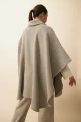 Poncho de lana fina sin teñir, con cuello camisero, cartera con broches a presión y bolsillo ojal. Diseño de estilo campestre con textura tejida.