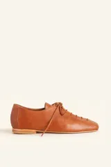 Zapato tipo oxford de cuero vacuno color whisky, con diseño de cordones laterales y suela plana de cuero.