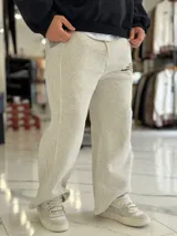 Pantalón de jogging oversize negro con felpa, de corte recto y cordón ajustable en la cintura. Presenta un pequeño estampado de texto blanco en el lateral izquierdo.