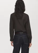 Blusa de color marrón oscuro con textura, cuello alto envolvente con detalle de fular integrado, manga larga con puños abotonados y diseño recto.
