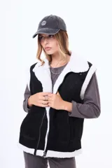 Chaleco estilo gamulán de color negro con interior y bordes de corderito blanco. Presenta cierre frontal, cuello solapa y bolsillos laterales.