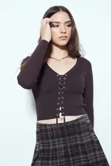 Top de tejido acanalado color negro, con escote en V y cierre frontal mediante cordones ajustables con ojales metálicos. Presenta mangas largas y un corte entallado al cuerpo.