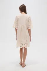 Vestido corto color crema, con escote en V y mangas 3/4. Presenta detalles de bordado inglés (broderie) en el canesú superior y en el ruedo inferior.