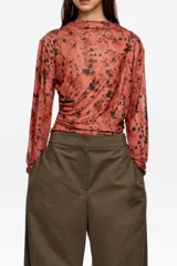 Camiseta de manga larga confeccionada en tejido de tul semitransparente con estampado animal print abstracto. Presenta cuello redondo, corte ajustado y detalles de frunces laterales que aportan textura y movimiento a la prenda.