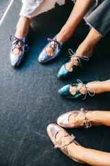 Zapato tipo blucher con diseño híbrido de bailarina, confeccionado en piel azul con textura de reptil. Presenta cierre con cordones y borlas de piel, con una banda elástica en la parte trasera para un ajuste óptimo. Cuenta con suela de cuero y acabado artesanal.