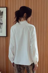 Camisa a rayas verticales rojas y blancas con cuello mao y mangas 3/4 abullonadas. Presenta detalles de puntilla blanca en el canesú. Cierre frontal con botones.