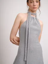 Vestido corto color marrón, con escote halter y tiras largas que se anudan al cuello estilo choker. Presenta un diseño con jareta en el escote y falda acampanada.