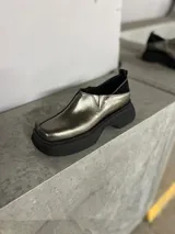 Zapato tipo mocasín color peltre con detalle de costuras en contraste y suela track color negro.