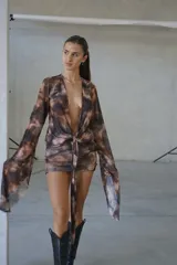 Vestido corto de tul con estampado batik en tonos marrones y negros. Presenta un escote profundo en V, mangas largas acampanadas y un detalle de nudo frontal con lazo que ajusta la cintura.