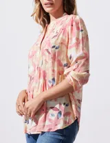 Blusa de gasa estampada con flores en tonos rosa, amarillo y azul. Tiene cuello a la base, escote en V y botones. La delantera tiene detalle plisado y las mangas son 3/4 regulables con presilla y botón.