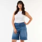 Bermuda vaquera de tiro alto con diseño amplio tipo bermuda, confeccionada en denim azul con lavado medio. Cuenta con cierre de botón y cremallera, y bolsillos delanteros y traseros clásicos.