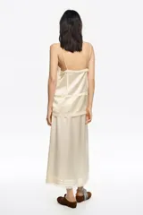 Falda midi de corte línea A en color beige, confeccionada en acetato. Presenta cremallera lateral invisible, bolsillos de plastrón y detalle de encaje a tono en el bajo.