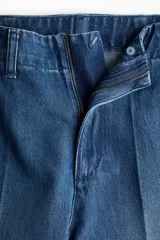 Pantalón de jean de tiro alto con corte wide leg y piernas amplias. Presenta diseño con raya frontal marcada, cierre con botón oculto, bolsillos laterales al bies y bolsillos traseros decorativos.