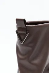 Bota de caña baja color negro, confeccionada en poliuretano con acabado liso y estructura flexible que genera un efecto fruncido. Presenta puntera redondeada, base baja y un cierre metálico en la parte trasera de la caña.