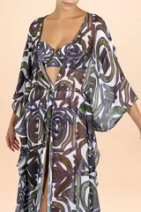 Caftán largo de estilo cover up, confeccionado en tela semitransparente con estampado botánico abstracto en tonos verde oliva y púrpura. Presenta mangas amplias tipo kimono, escote en V y cierre frontal con cordón ajustable en la cintura.