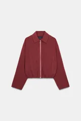 Cazadora tipo bomber color bordó, confeccionada en mezcla de viscosa. Presenta cuello solapa, manga larga, bolsillos de vivo laterales y bajo elástico. Cierre frontal con cremallera metálica.