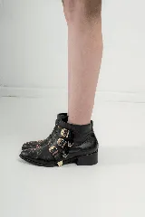 Botas cortas de cuero negro con puntera fina, taco bajo y cierre lateral. Presentan tres correas con hebillas plateadas y apliques de tachas plateadas.