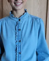 Camisa de jean azul con cuello alto con volados y volados en el frente.