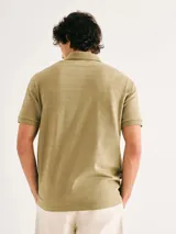 Camiseta tipo polo de manga corta en color verde, con diseño de rayas horizontales texturizadas en el tejido. Presenta cuello clásico, cierre frontal con dos botones y un pequeño detalle bordado en el pecho.